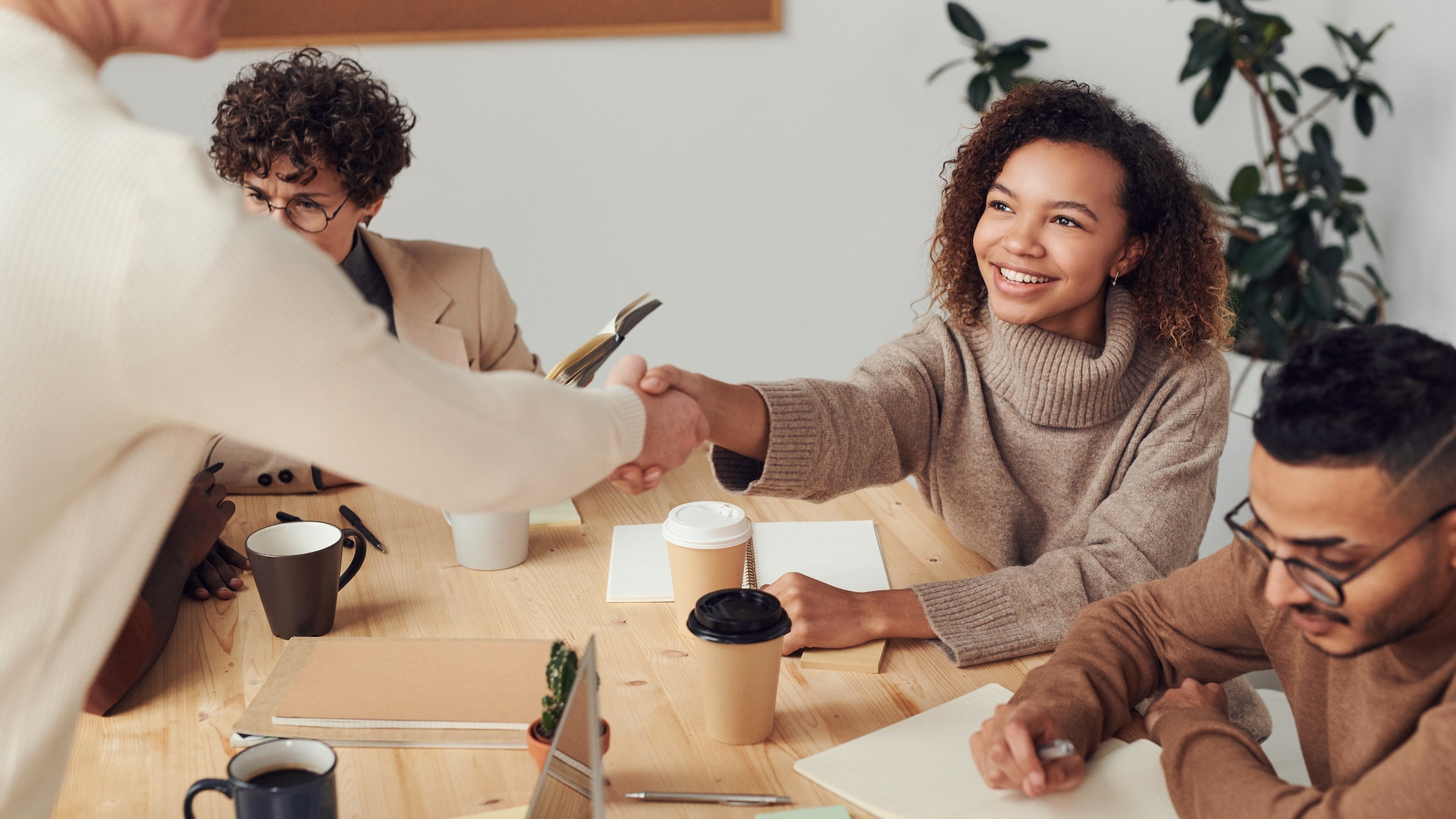 A group of real estate agents sit round an office table with two shaking hands and smiling